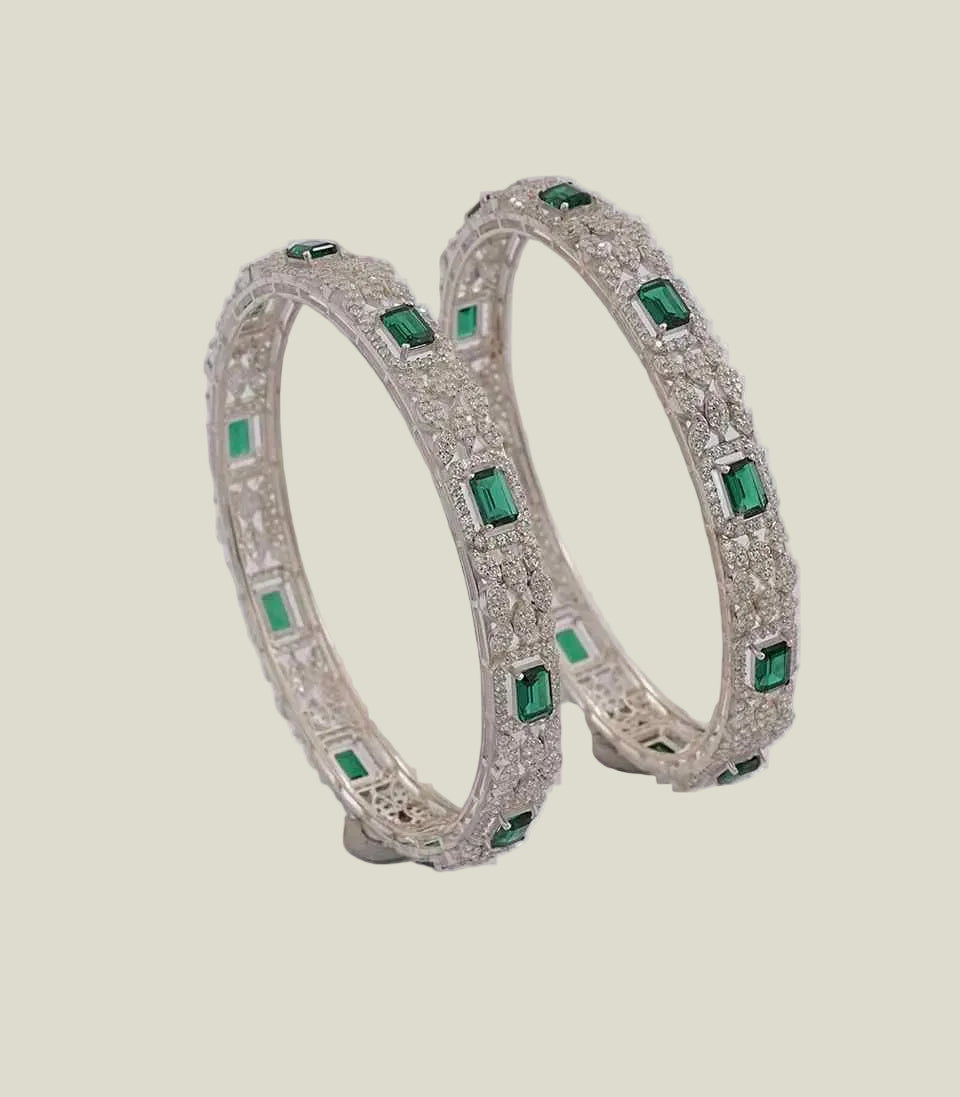 diamond bangles featuring emerald-cut emeralds set within a detailed geometric framework of sparkling diamond pave.