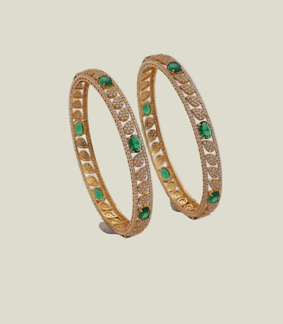 Pair of gold bangles with green gemstones on a light background