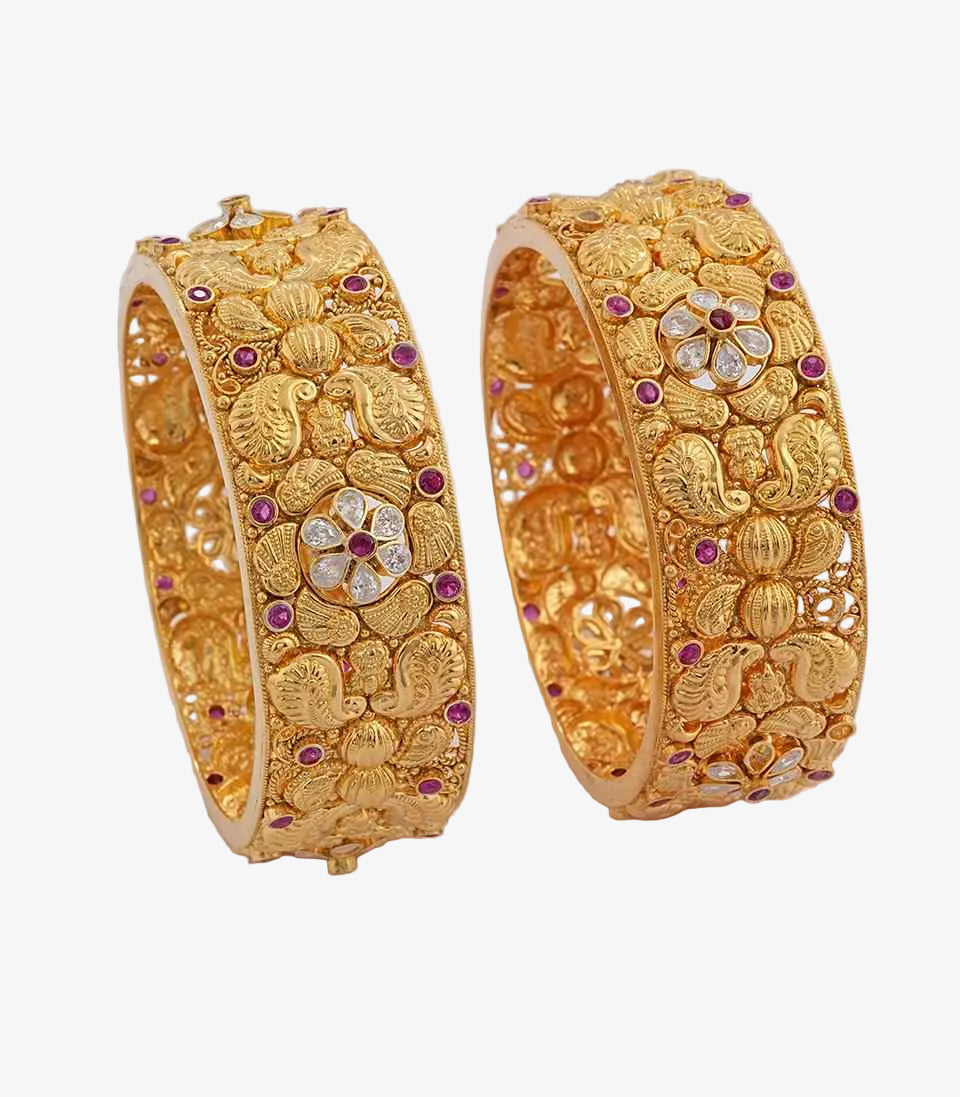 Pair of gold bangles with floral designs and gemstones on a white background