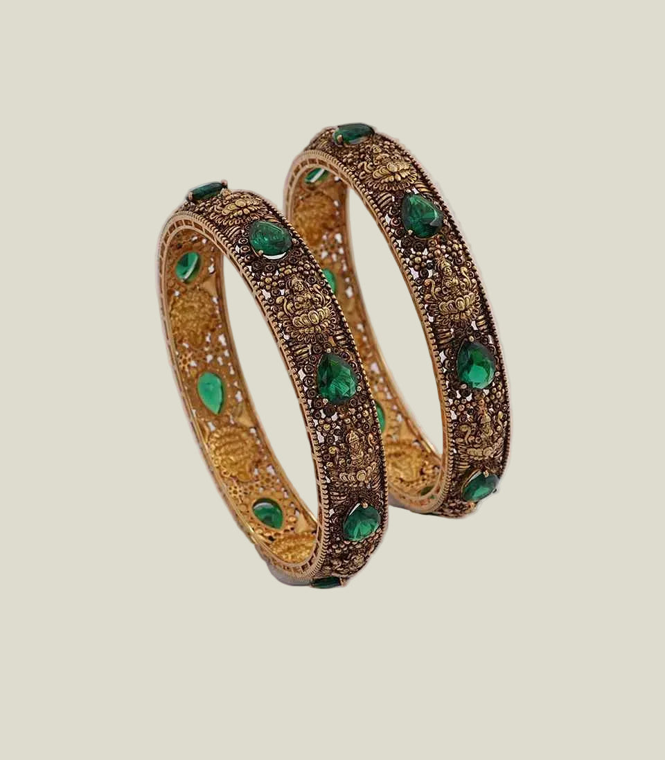 Pair of gold bangles with green gemstones on a white background