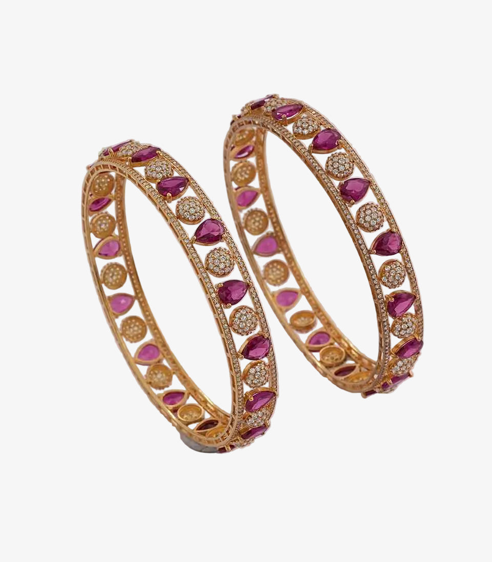 Pair of gold bangles with pink stones on a light background