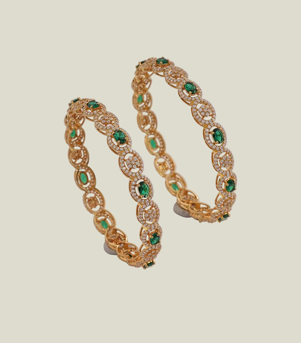 luxurious gold bangles featuring alternating oval emerald-green stones and floral motifs, all encrusted with a halo of sparkling white stone pave.