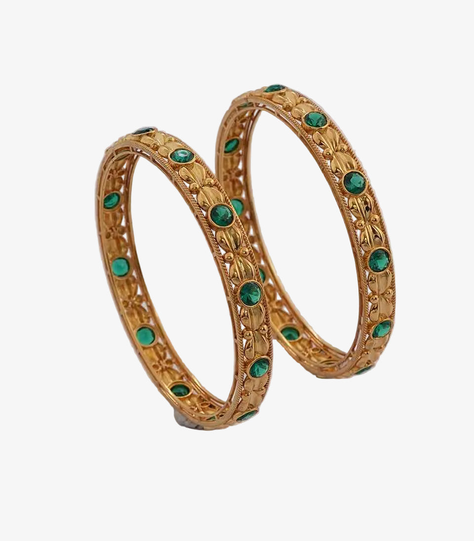 Pair of gold bangles with green gemstones on a white background