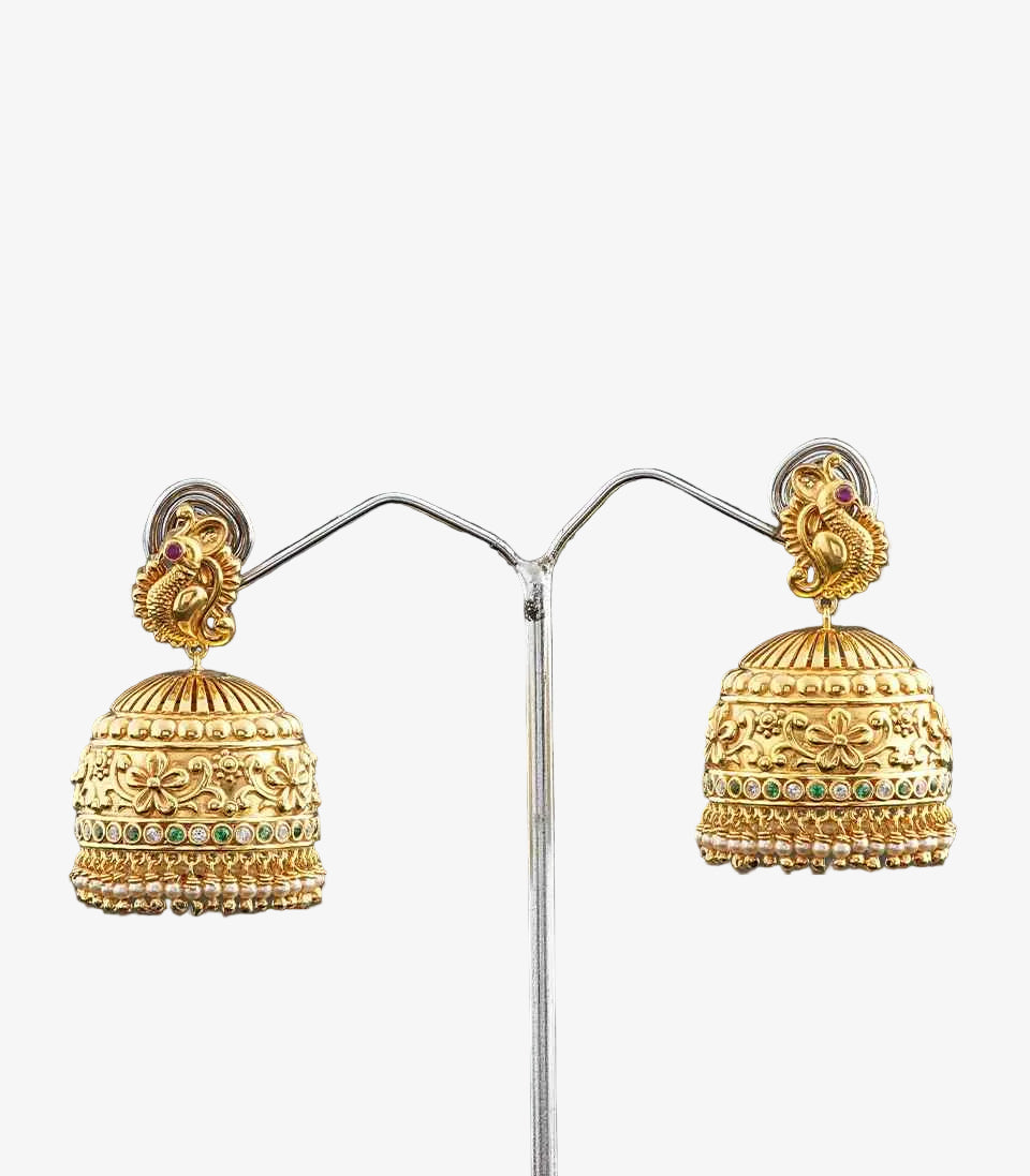 Gold jhumka earrings with peacock design on a stand against a dark background