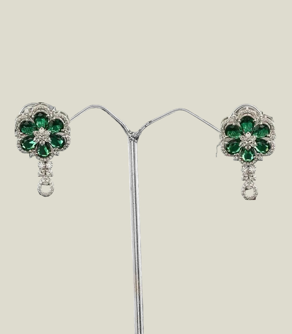 Pair of emerald and diamond earrings on a stand against a dark background