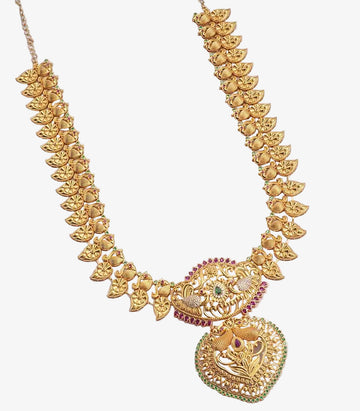 A long gold haram featuring a large circular pendant with peacock and floral engravings, accented with red and green stones, attached to a traditional manga malai chain of textured paisley motifs.