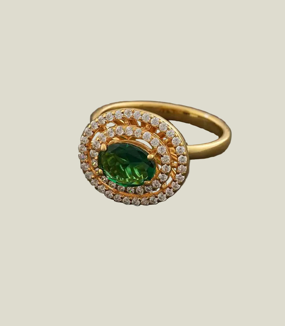 Gold ring with a green gemstone and diamond accents on a gray background