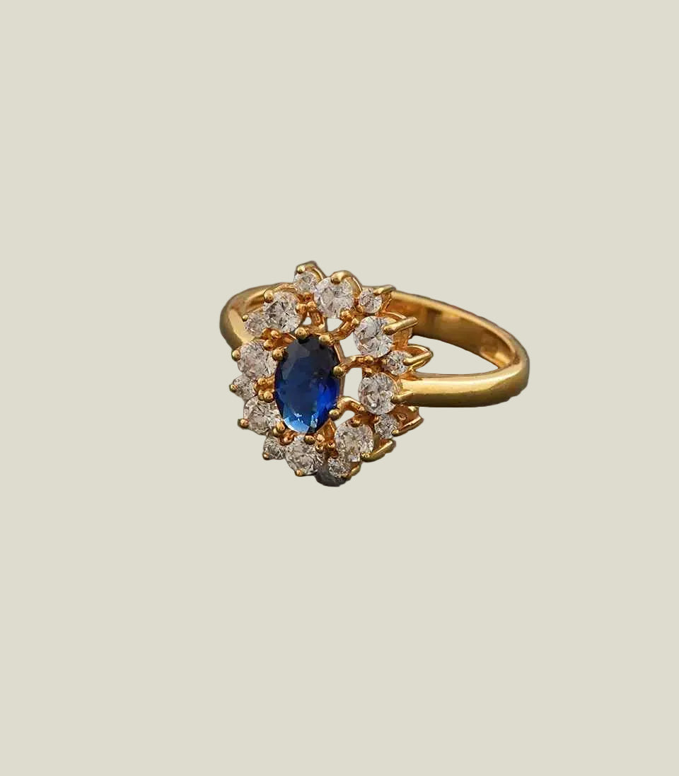 Gold ring with a blue gemstone and diamond accents on a gray background