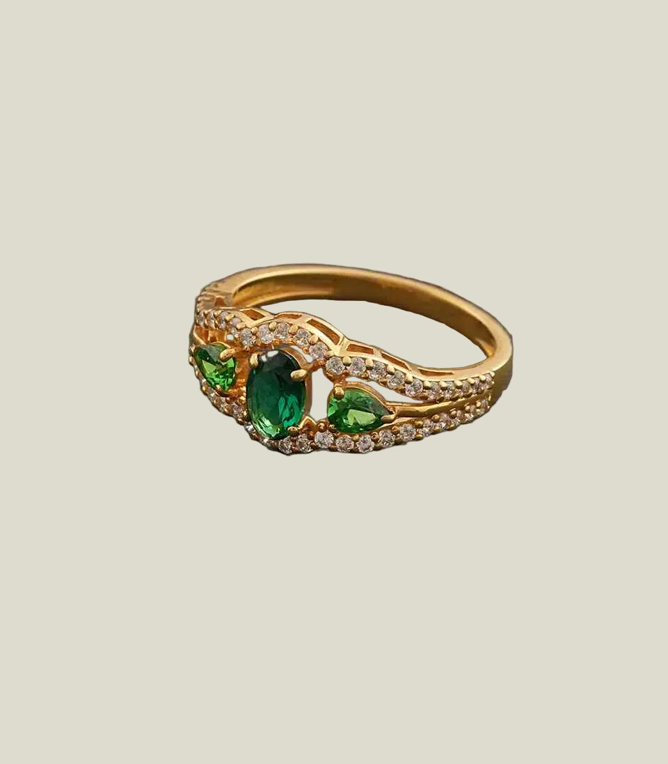 Gold ring with green gemstones on a gray background
