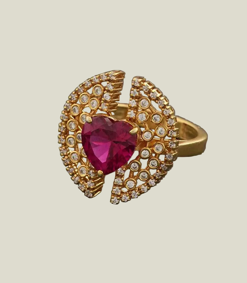 Gold ring with a heart-shaped ruby and diamond accents on a dark gray background